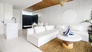 Una sala de estar moderna con un sofá blanco, una mesa de centro y una zona de cocina al fondo.
