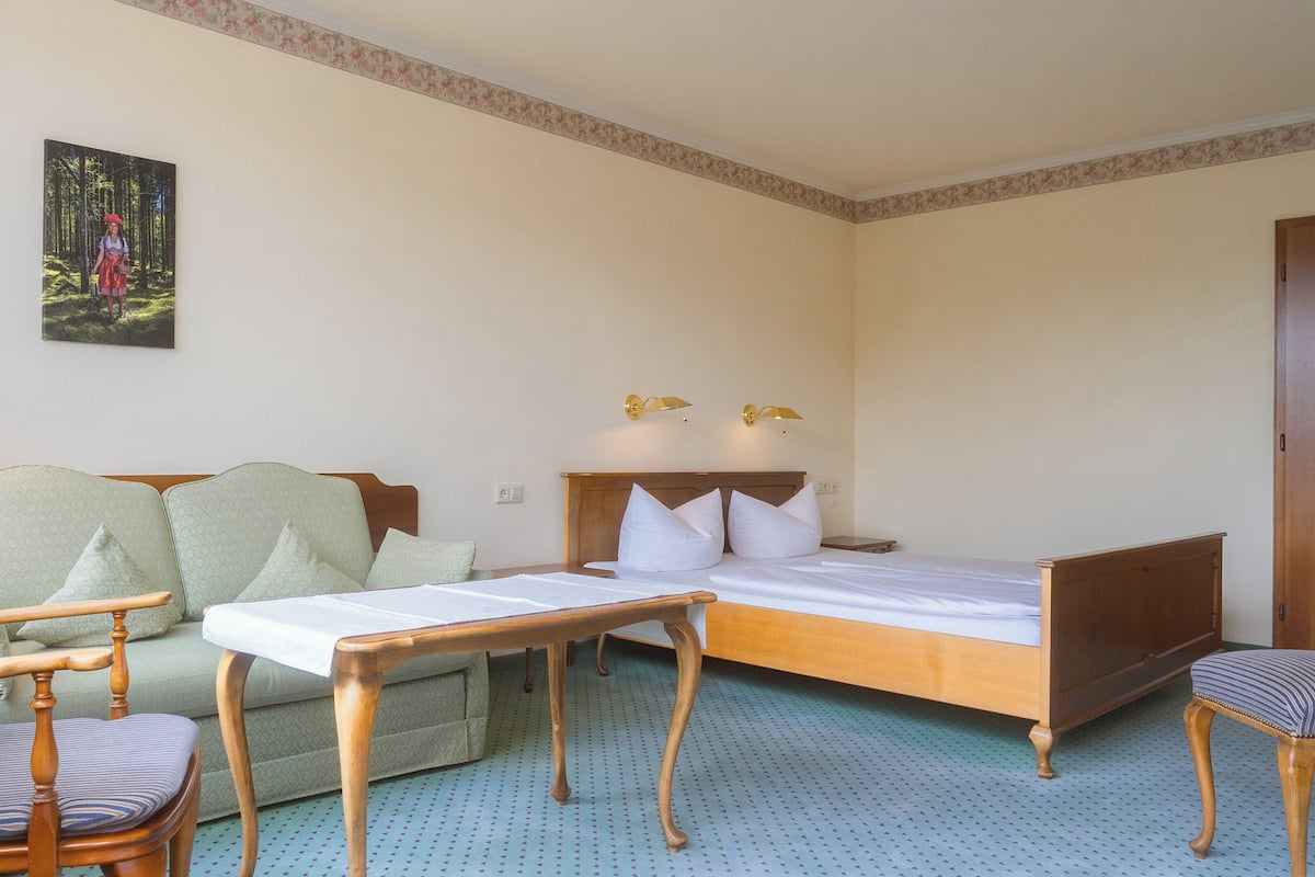 A hotel room with a bed, a desk, a chair, a sofa, and a painting on the wall.