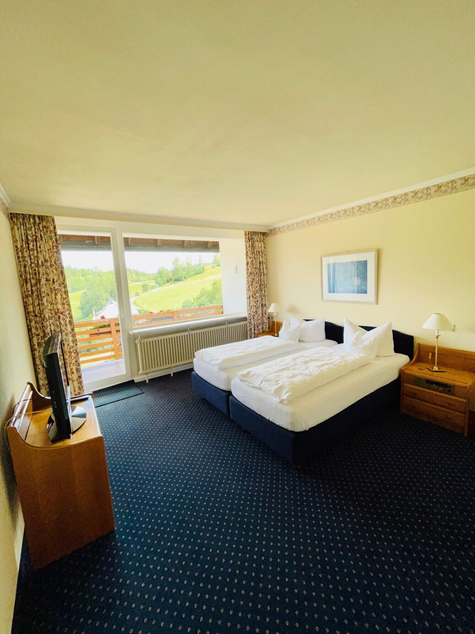 A hotel room with a large bed, a desk with a computer, a window with curtains, and a view of the outdoors.