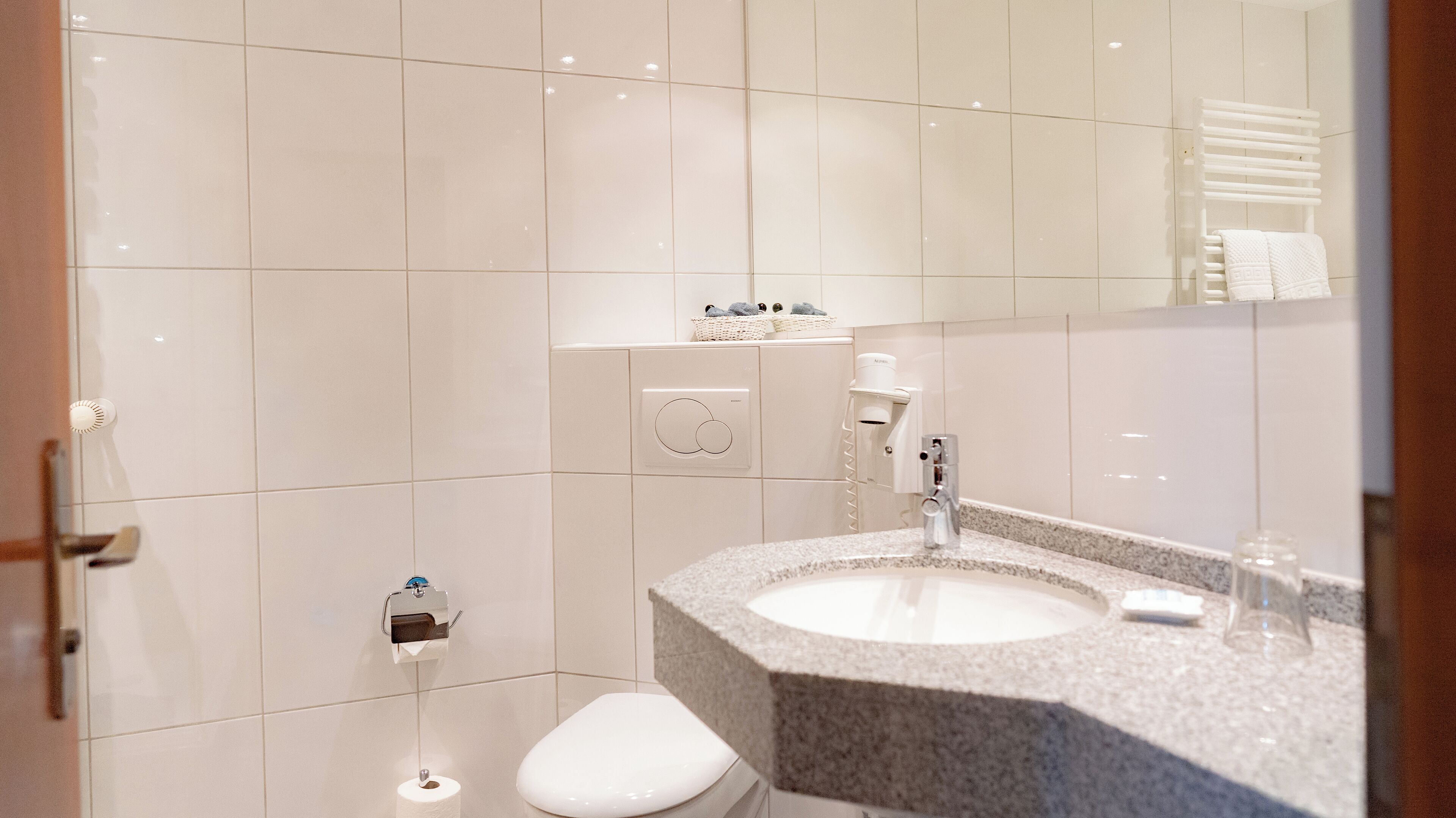 Un baño moderno con inodoro blanco, lavamanos de granito y un perchero para toallas.