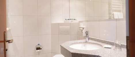 Un baño moderno con inodoro blanco, lavamanos de granito y un perchero para toallas.