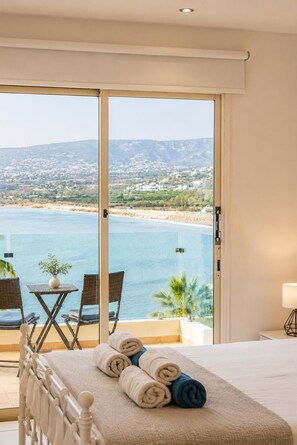 Une chambre d’hôtel avec un lit, un balcon donnant sur la mer et une table avec des chaises.