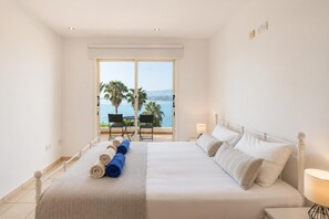 Une chambre d’hôtel avec un grand lit, une vue sur la mer et un balcon équipé de chaises.