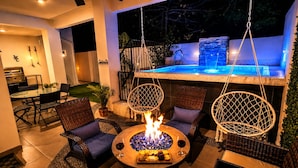 Un patio al aire libre con un brasero, sillas de mimbre, una mesa de comedor y una zona de piscina.