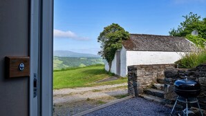 A view from a room with a door leading outside, a stone wall, and a barbecue grill. - Red Kites Retreat (Eglwysbach)