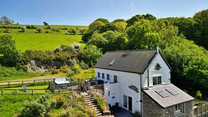 A white house with a stone foundation, a balcony, and a view of a green field and trees. - Red Kites Retreat (Eglwysbach)