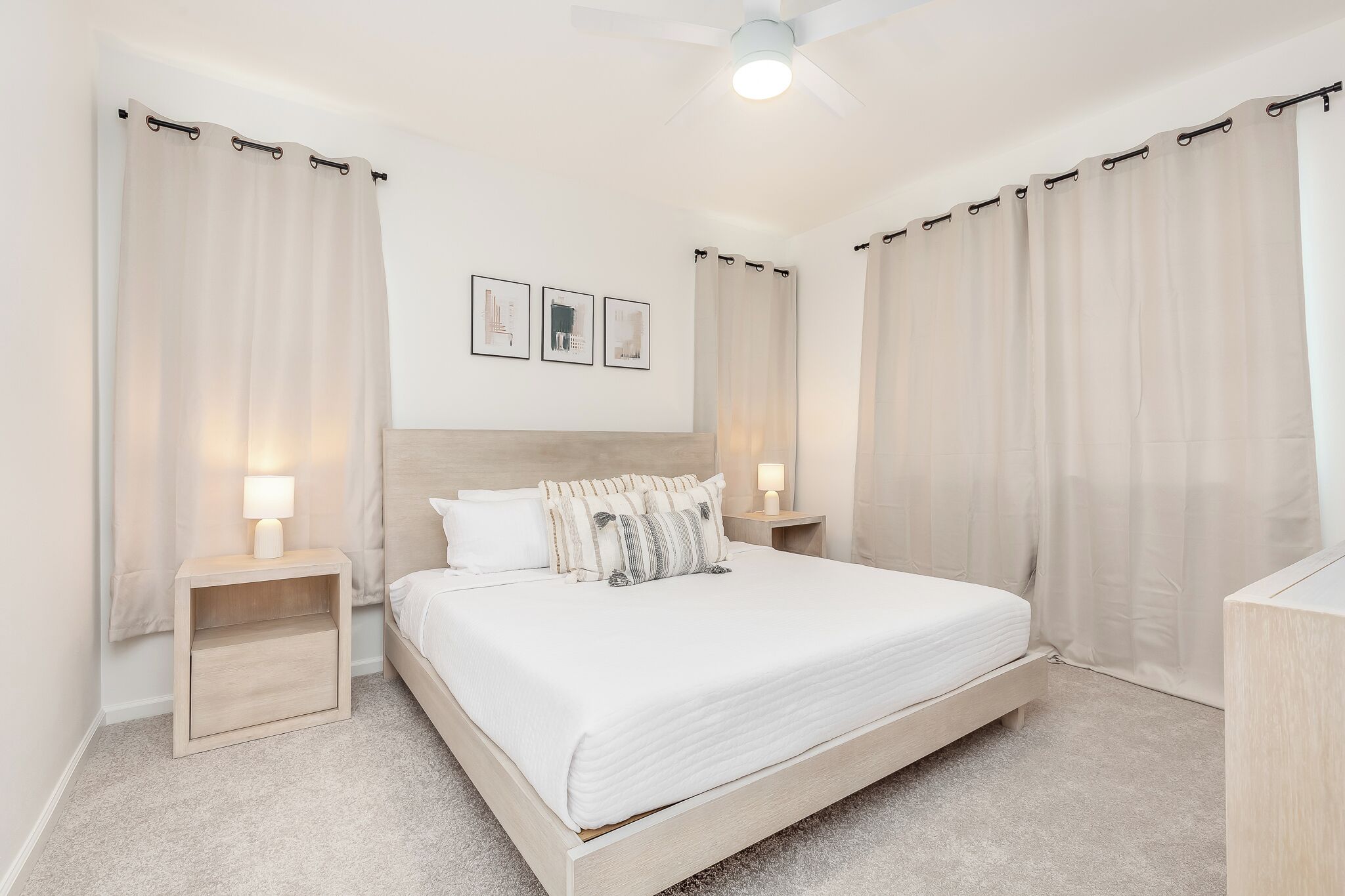 Ein Schlafzimmer mit Bett, Nachttischen, Deckenventilator und Vorhängen.