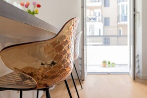 A modern interior with a reflective metallic chair, a wooden table, and a balcony with a view of buildings.