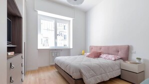 A bedroom with a bed, a nightstand, a dresser, and a window with blinds. - Design Premium apartment in center Milan-HomeUnity (Milano)