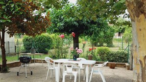 A patio with a white table and chairs, surrounded by greenery and a tree with pink flowers.