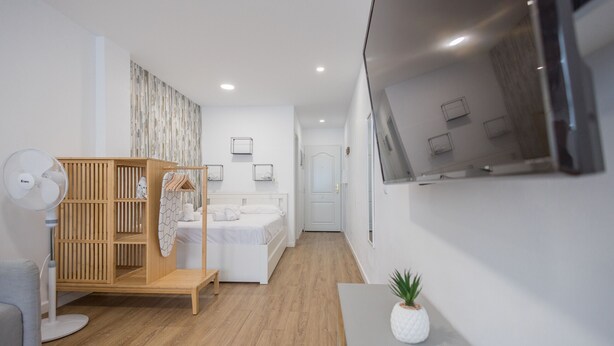 A modern, well-lit room with a wooden wardrobe, a bed, a small table with a plant, and a wall-mounted TV. - Las Canteras Beach - Bright Studio - Workfriendly (Las Palmas de Gran Canaria)