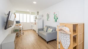 A modern, well-lit room with a grey sofa, a wooden cabinet, a flat-screen TV, and a window providing natural light. - Las Canteras Beach - Bright Studio - Workfriendly (Las Palmas de Gran Canaria)