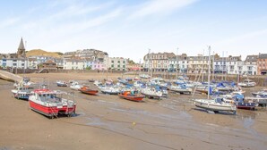 A coastal town with a marina filled with boats, buildings in the background, and a clear sky.