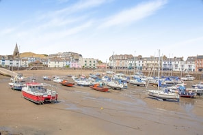A coastal town with a marina filled with boats, buildings in the background, and a clear sky.