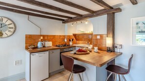 A compact kitchen with a wooden countertop, a small refrigerator, and a dining area with two stools.