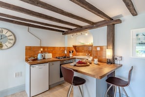 A compact kitchen with a wooden countertop, a small refrigerator, and a dining area with two stools.