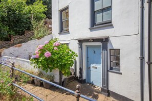 Un bâtiment blanc avec une porte bleue, une petite fenêtre et une rambarde en métal.