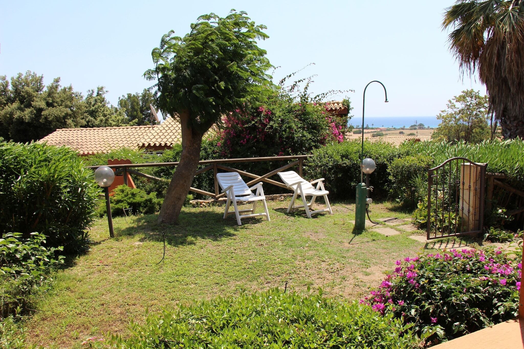 Un jardin avec deux chaises longues blanches, un arbre et une vue sur la mer.