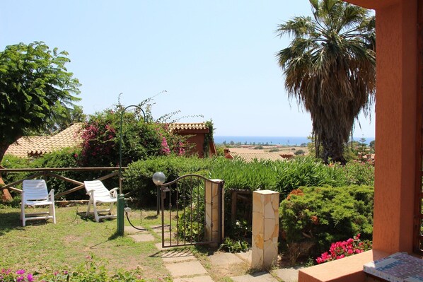 A garden with a view of the sea, a palm tree, and a house with a tiled roof.