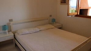 Habitación individual con una cama de madera, una mesita de noche con lámpara y una ventana con vistas al exterior.