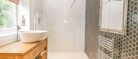 A bathroom with a white sink, wooden vanity, and a shower area with a glass door.