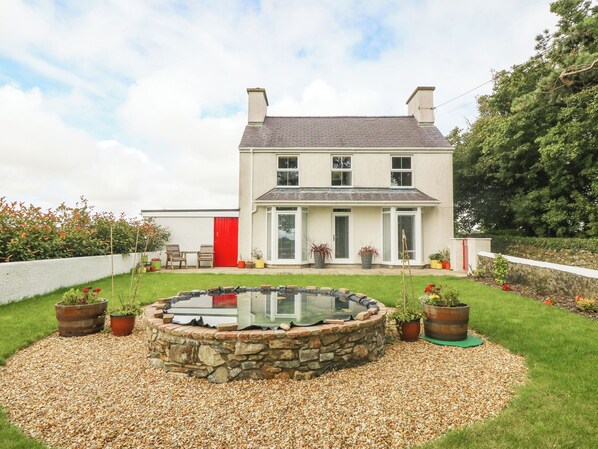 A two-story house with a stone swimming pool, surrounded by a gravel path and potted plants. - Bryn Tirion (Holyhead)