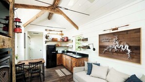 Une cuisine rustique avec des meubles de rangement en bois, un réfrigérateur noir et un coin repas comprenant une table et des chaises.