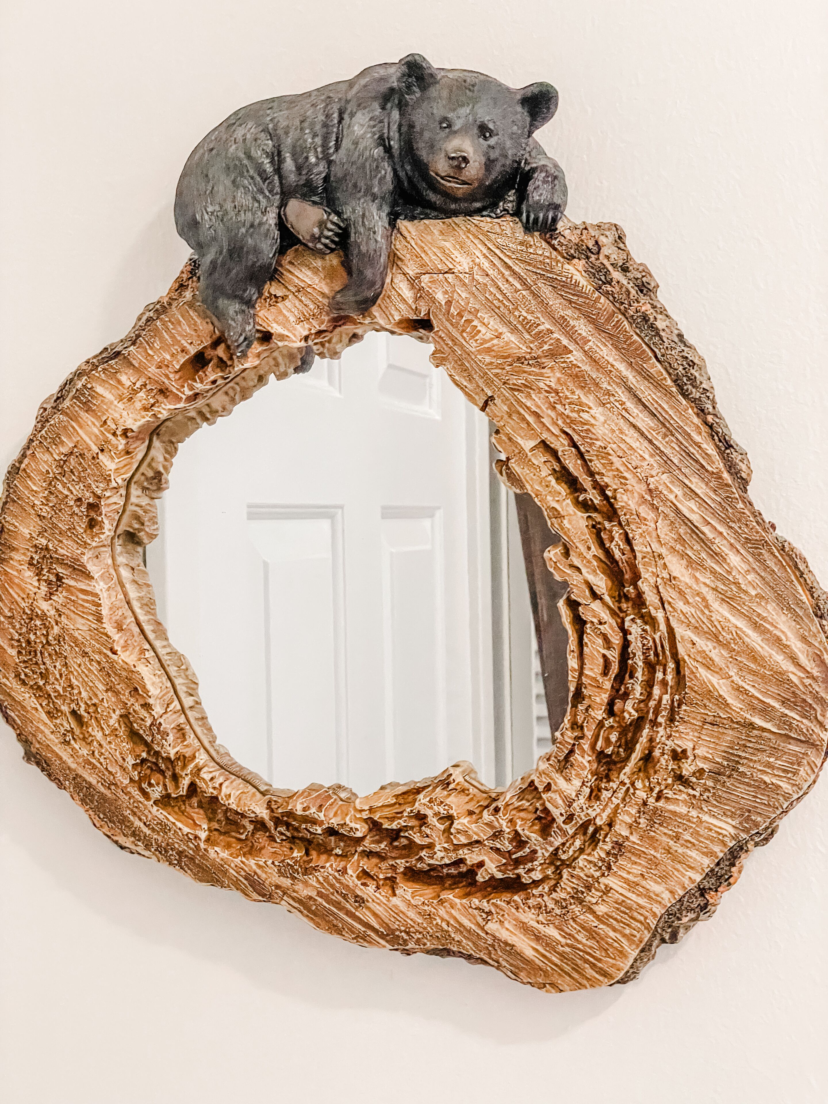 Une figurine d’ours posée sur un miroir rond à la texture particulière, dont le cadre est en bois brut.