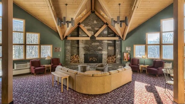 A cozy living room with a stone fireplace, wooden beams, and large windows. - Condo with loft near Loon mountain with pool/jacuzzi & free shuttle! (Lincoln)