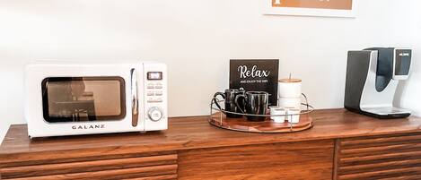 A wooden cabinet with a microwave, a coffee machine, and a tray with mugs and a sign that says "Relax and enjoy the WiFi."