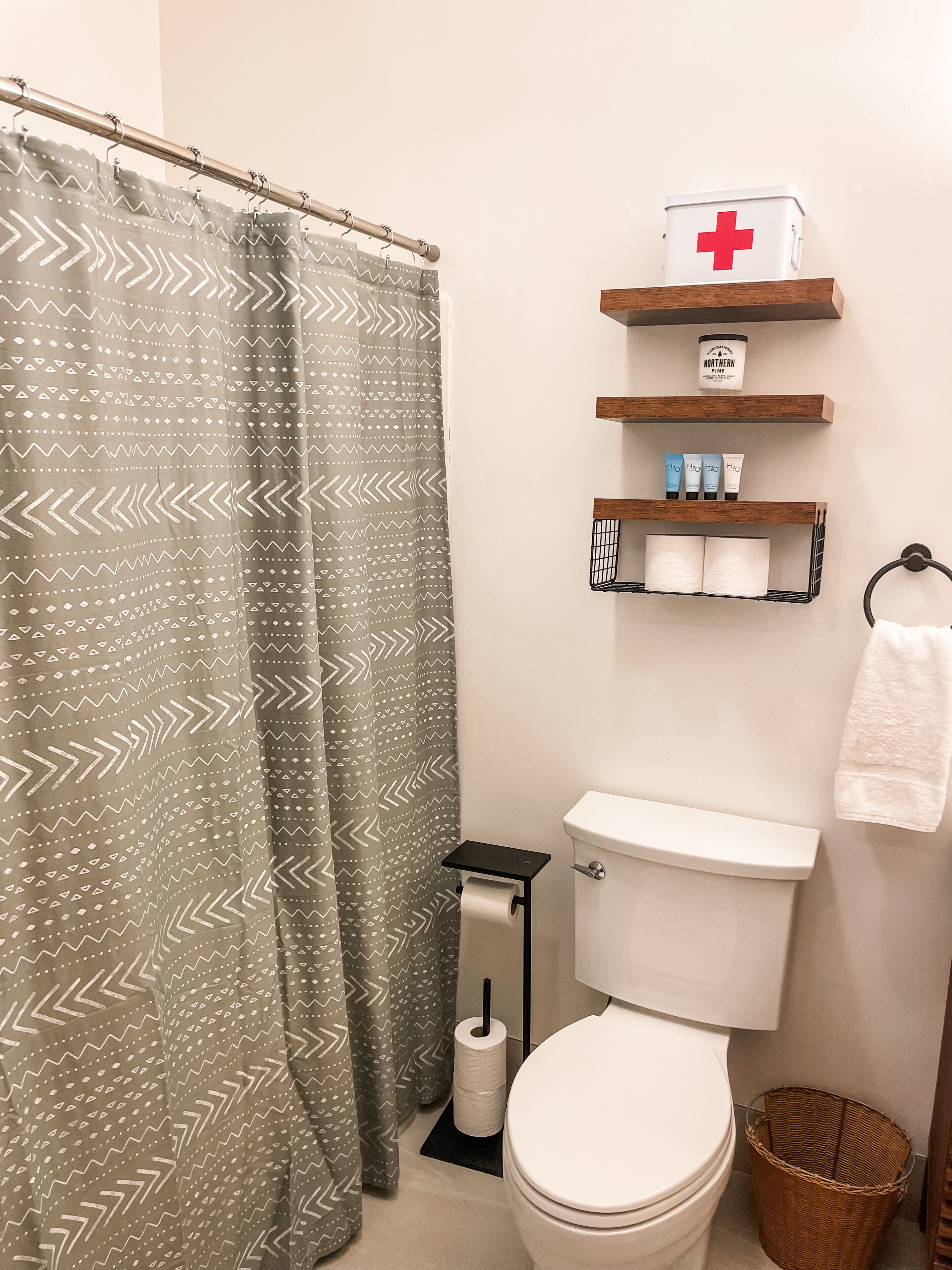 A bathroom with a shower curtain, toilet, and shelves with toiletries and a first aid kit.