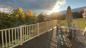 A deck with a table and chairs, overlooking a garden with trees and a building in the background. - Condo with loft near Loon mountain with pool/jacuzzi & free shuttle! (Lincoln)