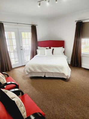 Ein Hotelzimmer mit einem großen Bett, einem roten Kopfteil und Blick durch das Fenster nach draußen.