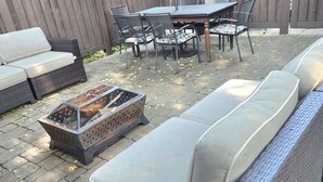 Une terrasse extérieure avec un canapé en osier, une table à manger avec des chaises et un barbecue.