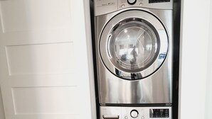 Un appareil combiné lave-linge et sèche-linge à chargement frontal, compact et en acier inoxydable, installé dans un espace étroit et doté d’une porte blanche.