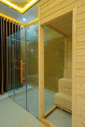 Relax in a serene sauna room with a glass door, wooden bench, and decorative lighting.