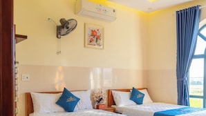 Une chambre d’hôtel avec deux lits, un ventilateur de plafond, un appareil de climatisation, une table de chevet et une fenêtre avec des rideaux.