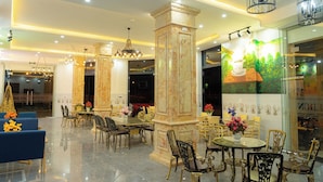 Un hall d’entrée bien éclairé, doté de colonnes en marbre, de lustres et d’un espace repas avec des chaises et des tables richement décorées.