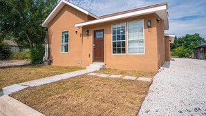 A single-story house with a brown exterior, a front door, and a small front yard with a gravel path. - Charming 3BR/2BA Gem Close to Downtown/ Riverwalk (San Antonio)