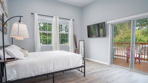 A bedroom with a bed, a nightstand, a lamp, two windows with curtains, a painting on the wall, and a view of the outdoors through a sliding glass door. - Charming 3BR/2BA Gem Close to Downtown/ Riverwalk (San Antonio)