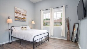 A bedroom with a bed, two bedside lamps, a window with curtains, a painting on the wall, and a TV mounted on the wall. - Charming 3BR/2BA Gem Close to Downtown/ Riverwalk (San Antonio)