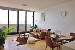 Relax in this stylish living room with a city view, featuring a comfortable sofa, dining area, and potted plant.