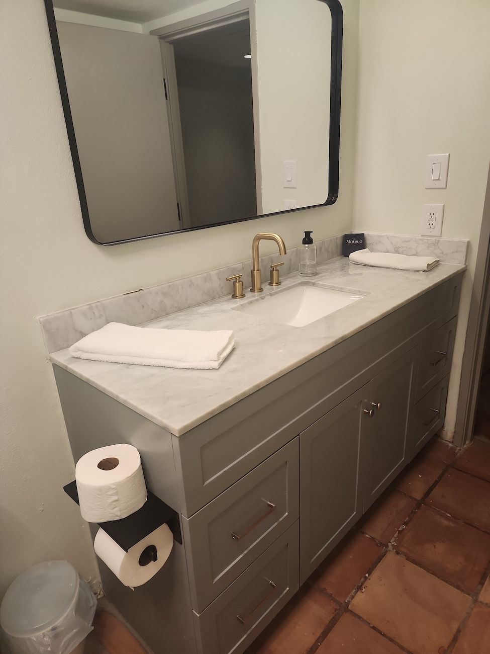 Un baño con lavamanos de mármol, un espejo grande y un dispensador de papel higiénico.