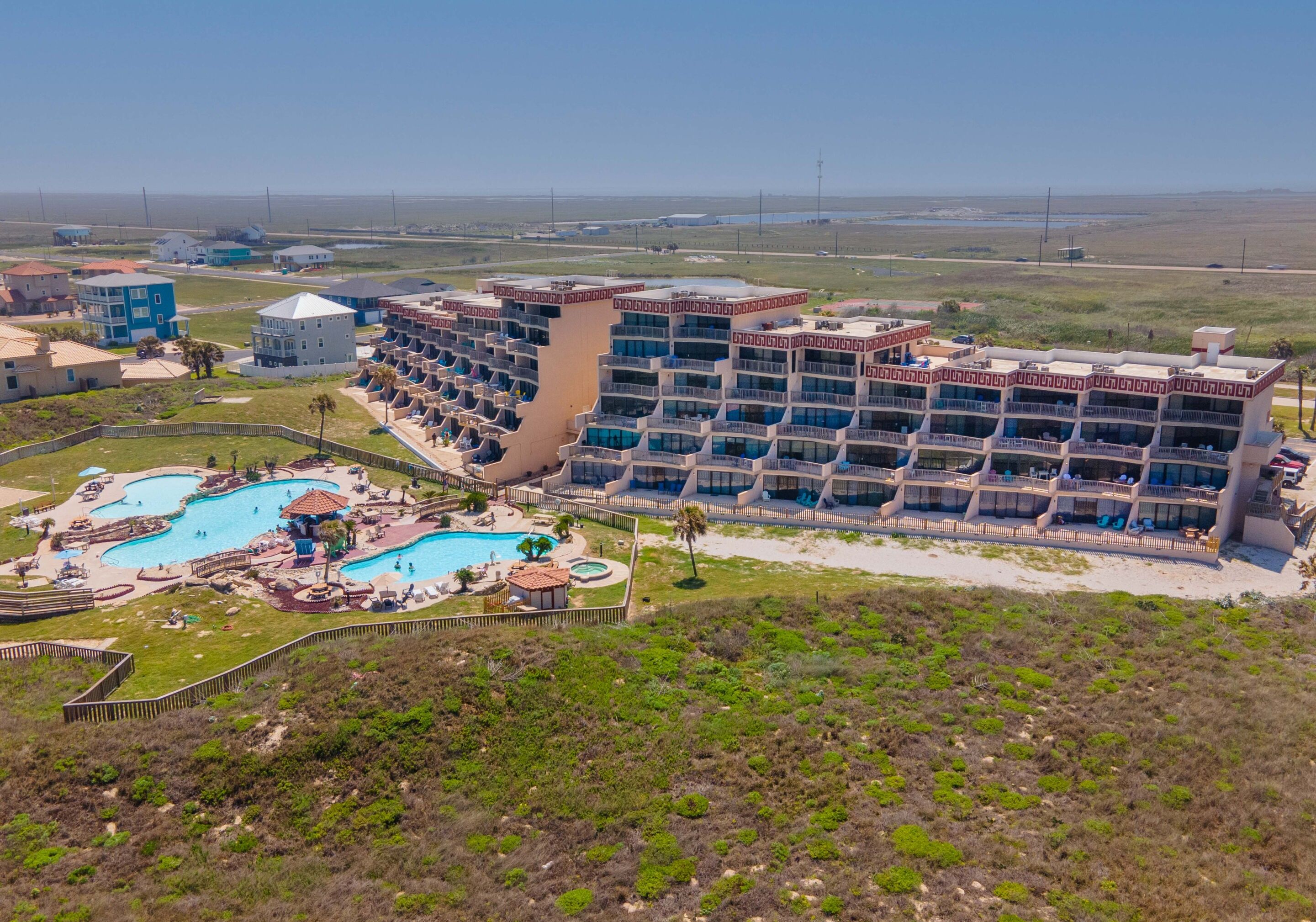 Un resort con varias edificaciones, una piscina grande y una zona de playa.