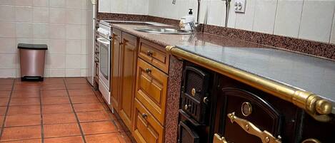 A kitchen with a tiled backsplash, wooden cabinets, a stainless steel sink, and a vintage-style oven.
