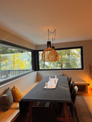 A modern dining area with a large window, a table with candles, and a hanging light fixture. - Chalet La Source (Nendaz)