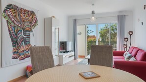 Een moderne woonkamer met een grote wandtapijt van een olifant, een rode bank en een eethoek met een ronde tafel.
