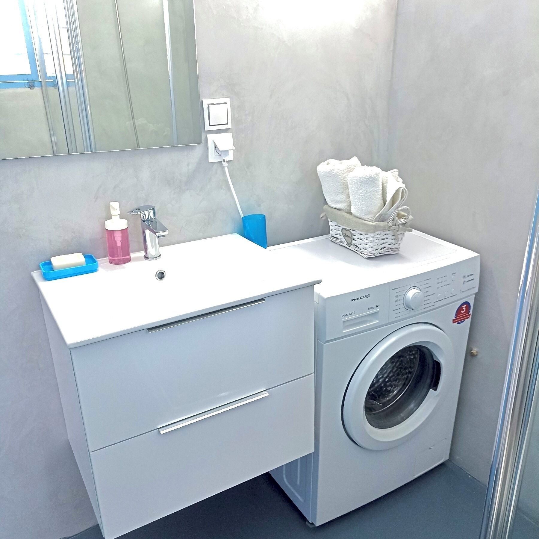 A compact bathroom with a white sink, a washing machine, and a mirror above the sink.