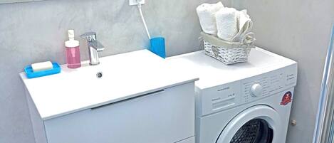 A compact bathroom with a white sink, a washing machine, and a mirror above the sink.