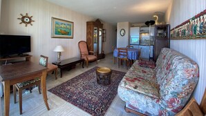 A living room with a sofa, a TV, a dining table, and a kitchen area.